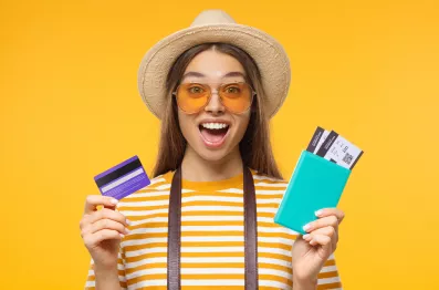 DirectAsia Insurance_female wearing a hat and yellow-striped tee, one hand holding passport (with boarding tickets), the other hand holding a credit card.